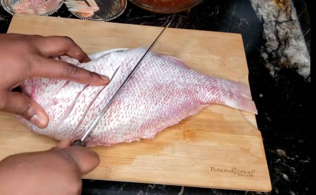 Cleaned and washed red snapper is slitting for marinating. 